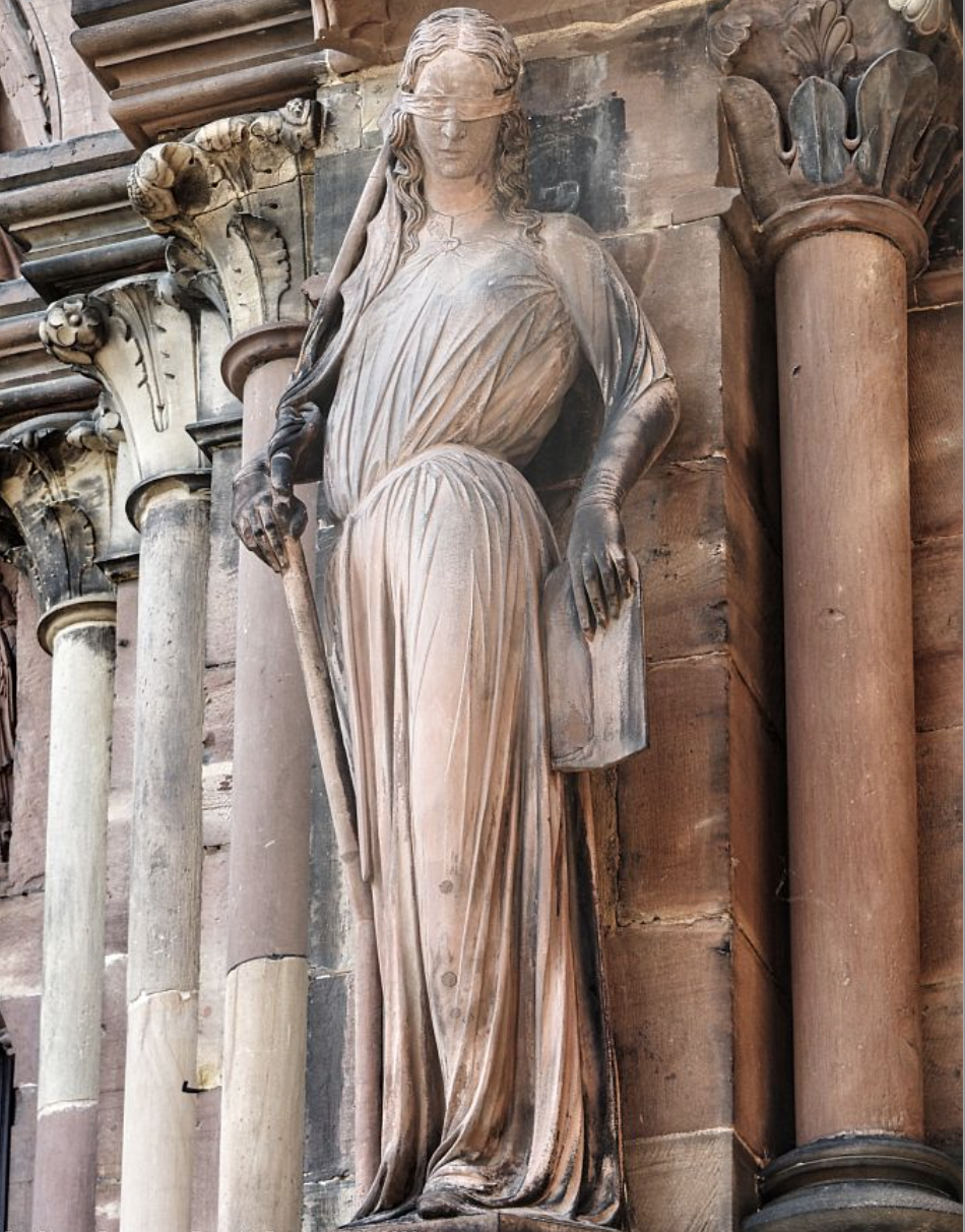 Steinerne Statue der Synagoga mit verbundenen Augen, Schwert und Buch an einer Säulenfassade
